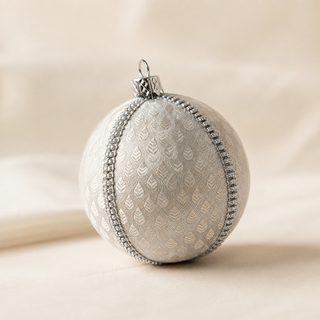 Surya bauble detail shot, an 8cm UK-made sustainable ornament with soft ivory ground and a woven brocade leaf motif with a fine silver diamanté trim.