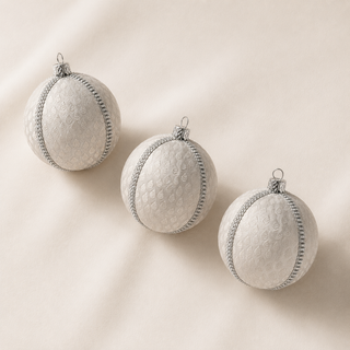 Surya handmade fabric bauble on a marble surface, 8cm, showing a woven brocade leaf motif with a fine silver diamanté trim on a soft ivory ground.