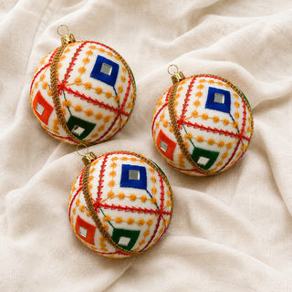 Close-up of the Sohan bauble showing bold red diagonal lines with a fine gold star-stitch pattern and mirror-centred diamonds on crisp white reclaimed fabric.