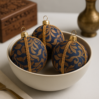 Decorative blue and gold ornaments in a white bowl on a neutral background. Handcrafted Vani Bauble in navy fabric with shimmering gold baroque pattern, UK-made.