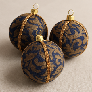 Three decorative Christmas ornaments with blue and gold patterns on a beige background. Vani Bauble – 8cm handmade fabric ornament in deep blue with ornate gold baroque embroidery, luxury sustainable décor.