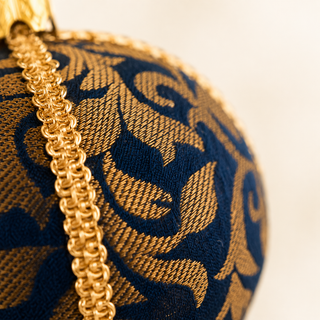 A cluster of Vani handmade fabric baubles, 10cm, grouped to show the sweeping gold floral scrollwork woven throughout with a gold cord seam trim.