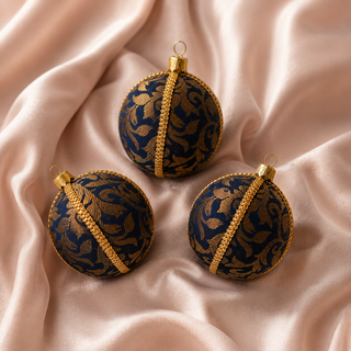 Vani bauble hanging with soft bokeh lights, showing its navy ground and sweeping gold floral scrollwork woven throughout with a gold cord seam trim.