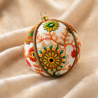Vanika fabric bauble styled on linen, an 8cm handmade ornament with embroidered floral medallions in orange, yellow, green and red with mirror-work centres and a gold cord trim.