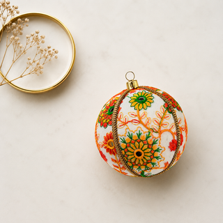 Vanika bauble detail shot, an 8cm UK-made sustainable ornament with cream ground and embroidered floral medallions in orange, yellow, green and red with mirror-work centres and a gold cord trim.