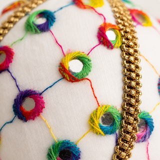Vikram fabric bauble styled on linen, an 8cm handmade ornament with a lattice of coloured thread with rainbow stitched circles and tiny mirror centres.