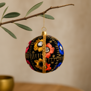 Decorative ornament with floral patterns hanging from a branch against a neutral background. Vimal Bauble – sustainable fabric decoration with colourful embroidery and reflective mirrors, handmade in the UK.