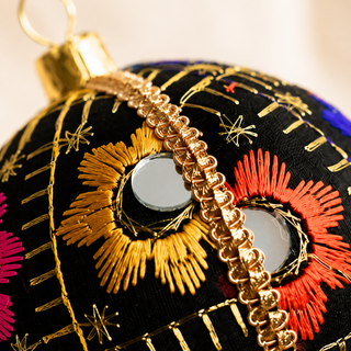 Vimal bauble detail shot, an 8cm UK-made sustainable ornament with black ground and bursts of gold, orange, pink and blue floral embroidery with mirror discs and gold quilted stitch lines.