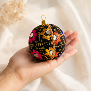 Vimal fabric bauble styled on linen, an 8cm handmade ornament with bursts of gold, orange, pink and blue floral embroidery with mirror discs and gold quilted stitch lines.