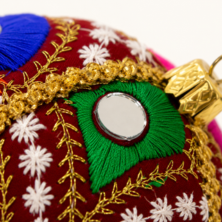 A cluster of Vivaan handmade fabric baubles, 8cm, grouped to show the densely embroidered peacock-feather motifs in green, pink, orange and blue with mirror-disc centres.