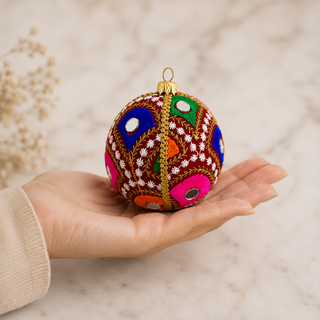 Vivaan bauble detail shot, an 8cm UK-made sustainable ornament with deep teal (also in maroon) ground and densely embroidered peacock-feather motifs in green, pink, orange and blue with mirror-disc centres.
