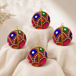 Close-up of the Vivaan bauble showing densely embroidered peacock-feather motifs in green, pink, orange and blue with mirror-disc centres on deep teal (also in maroon) reclaimed fabric.