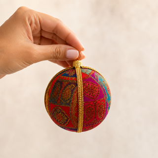 Yashodah bauble detail shot, a 10cm UK-made sustainable ornament with magenta, teal, purple and red patchwork panels ground and intricate gold paisley and medallion embroidery with a gold cord seam trim.