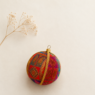 Yashodah fabric bauble styled on linen, a 10cm handmade ornament with intricate gold paisley and medallion embroidery with a gold cord seam trim.