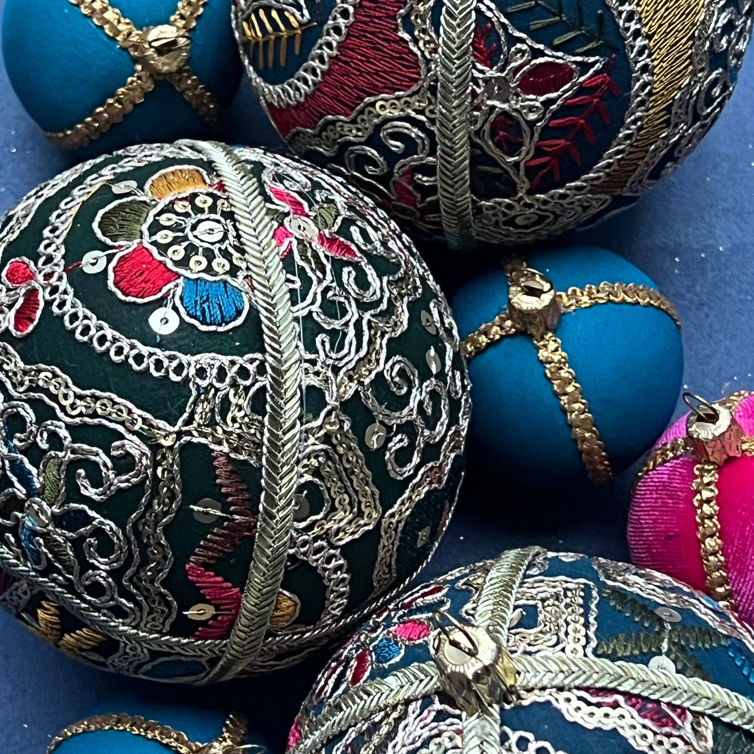 Square close-up of the Aaina Bauble in rich teal fabric with multicoloured embroidery and gold threadwork. Styled with smaller coordinating baubles for scale and texture.