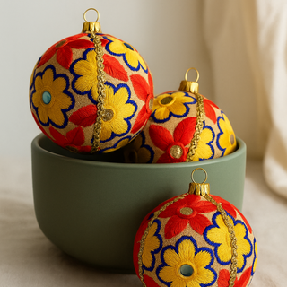 Decorative Christmas ornaments with advik floral patterns in a green bowl on a neutral background