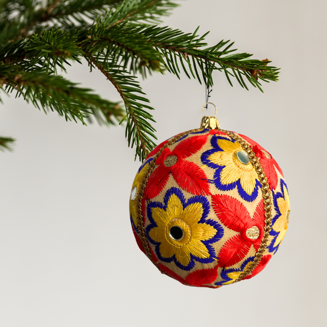 Decorative Advik Christmas ball ornament with floral patterns hanging on a tree branch.