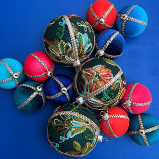 Flat lay of assorted handmade baubles including the Anung Bauble in 8cm, displayed on a bright blue background for a bold and festive look.