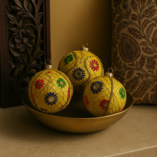 Set of three Aradhya Baubles placed in a brass bowl on a marble surface, surrounded by a carved wood panel and block print cushion, evoking refined Indian elegance.