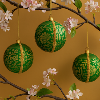 A cherry blossom tree branch displays three Bhav Baubles in deep green with gold brocade embroidery, hanging naturally to showcase their detailed craftsmanship.