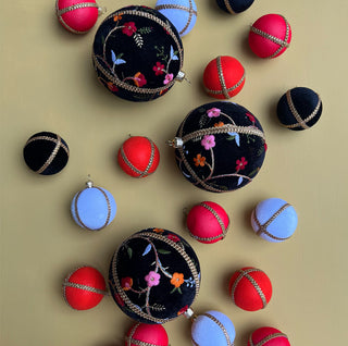 Flat lay of Kashvi Baubles in 10cm surrounded by smaller baubles in black, red, blue and pink velvet with gold trim, styled on a mustard background.