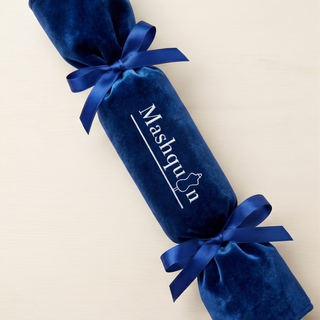 A royal blue velvet Christmas cracker ornament with a matching blue ribbon bow and white printed text reading 'Mashquin' on a light beige background.