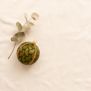 Charu fabric bauble styled on linen, an 8cm handmade ornament with a bold gold woven paisley brocade with a gold chain braid trim.