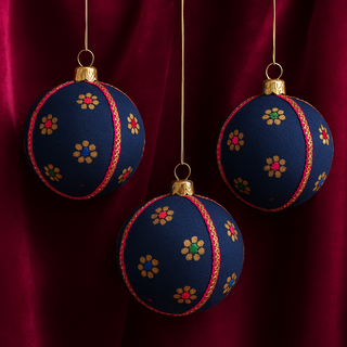 Three Dancing Flowers baubles resting on deep pink silk fabric, with a soft luxurious drape to highlight the colour pop and gold accents.