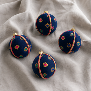 Dancing Florals bauble hanging with soft bokeh lights, showing its deep navy ground and scattered gold flower motifs with jewel-tone pink, green and blue centres.