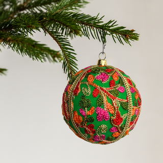 Decorative Daviki Christmas ball ornament with floral patterns hanging on a tree branch.