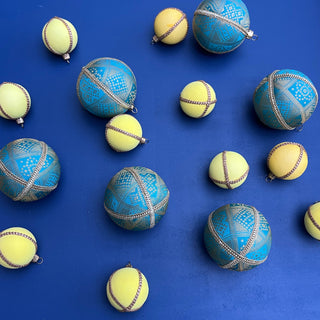 Flatlay of Hem Baubles in 8cm with turquoise fabric and gold motifs, styled with lemon yellow baubles on a deep blue background for a bold, modern look.
