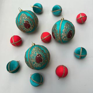 Flat lay featuring Himesh Baubles in 10cm with teal fabric, red paisley centre and gold embroidery, styled alongside red and teal velvet baubles on a soft grey background.