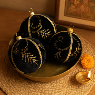 Three Kaia Baubles in 10cm rest in a brass bowl with a diya and marigold on a jute mat, styled with warm light and a framed Indian artwork in the background.