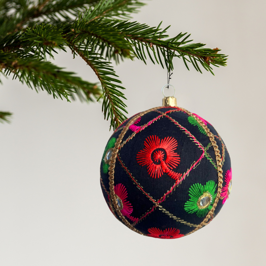 Decorative Kalyani Christmas bauble  ornament with colourful embroidery hanging on a tree branch. Luxury handmade bauble in black with multicoloured floral embroidery and mirrors, sustainable ornament for Christmas, Diwali, weddings, and gifting.