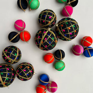 Flat lay of various velvet baubles including the 8cm Kimaya Baubles in black with bright embroidery and gold trim, surrounded by smaller colourful baubles on a white background.