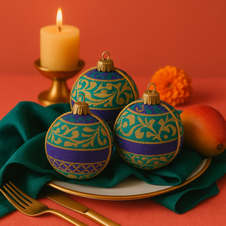 A colourful tablescape featuring three 8cm Krisha Baubles resting on a white plate with gold trim, styled with an emerald napkin, mango, candle and marigold for a vibrant, luxurious look.