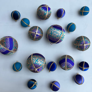 Flat lay of multiple fabric baubles in rich teal, blue, and purple tones with gold detailing, including several Krisha Baubles in varying sizes, styled on a pale blue background.