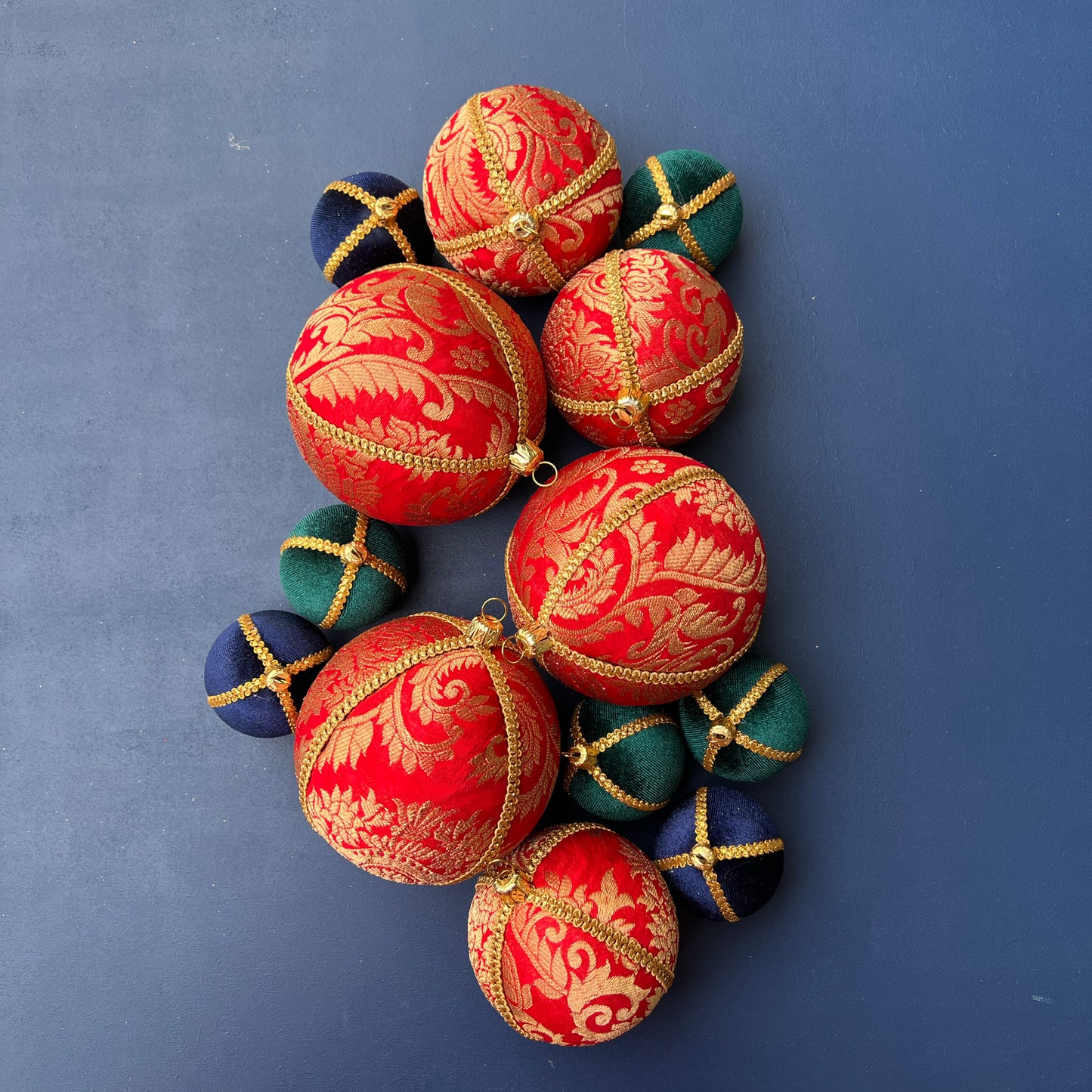 A group of Laksh Baubles in bright red with gold brocade, gold trim, and metallic caps laid flat on a deep blue background for a bold festive display.