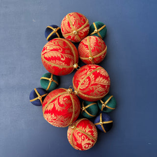 A group of Laksh Baubles in bright red with gold brocade, gold trim, and metallic caps laid flat on a deep blue background for a bold festive display.