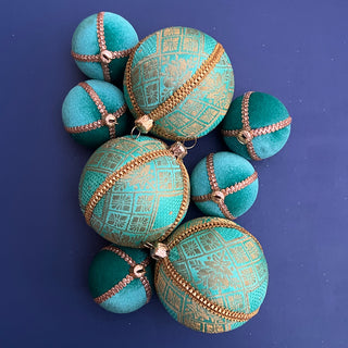 A collection of turquoise baubles, including the Lakshmanji Bauble with gold brocade, surrounded by coordinating plain velvet baubles on a deep blue background.