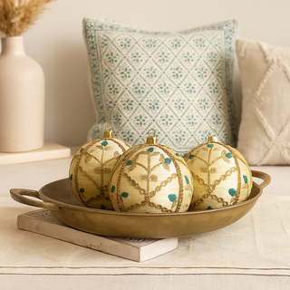 Lalit Baubles displayed in a brass tray atop a cream surface, with carved wood, neutral textiles, and teal block-printed cushions in a calm Indian-inspired home.