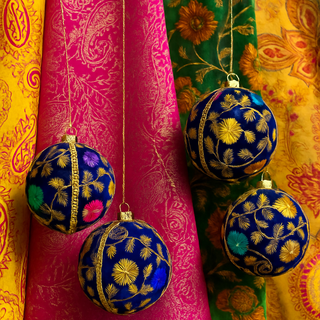 Four Mahir Baubles hanging against layered embroidered fabrics in vibrant jewel tones, creating a bold and boho-luxury editorial scene.