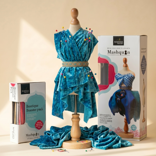 Mashquin fashion design kit for children — teal fabric draped on tabletop mannequin with dressmaking pins, shown with product box and boutique booster pack