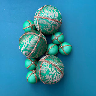 A bold and playful flatlay of Nalin Baubles in green and gold, mixed with coordinating green velvet designs, styled against a bright blue background.