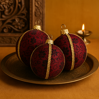 Three Nimit Baubles resting on an engraved brass tray with a carved wooden panel and a glowing diya, styled against a mustard background.