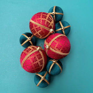 A set of decorative Christmas ornaments shaped like spheres, featuring a mix of deep red and teal blue fabrics with gold patterns and trim, arranged on a solid teal background.