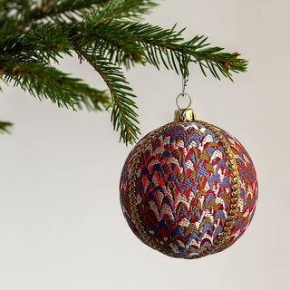 Decorative Christmas ball ornament with intricate pattern hanging on a tree branch.