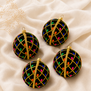 Four black Christmas ornaments with gold lattice patterns and colorful neon light dots, arranged on a cream fabric background.