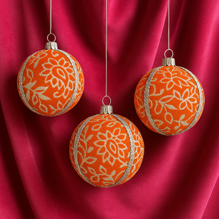 Three Shylah Baubles hanging against draped fabric, featuring bright orange brocade with silver floral detailing and silver trim, styled with warm lighting.