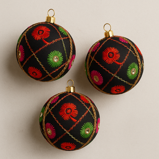 Three black Kalyani embroidered Christmas ornaments with colorful patterns on a beige background. Handcrafted Kalyani Bauble in black fabric with gold lattice embroidery, floral detailing, and mirror accents, UK-made.